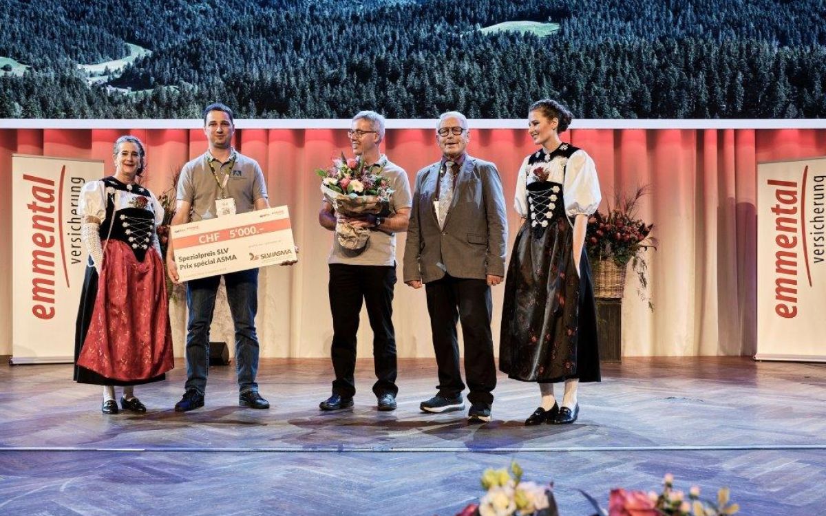 Stefan Isaak, Landmaschinenmechaniker und Maschinenbautechniker HF (2. v. li.), und Markus Ryser, Geschäftsinhaber (3. v. li.), auf der Bühne im Berner Kursaal. Bendicht Hauswirth vom SLV (2. v. r.) überreicht die Auszeichnung und den symbolischen Scheck über 5'000 CHF.